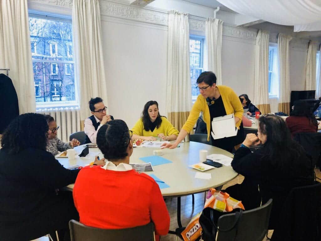 a group of people working together at a table with a facilitator handing out papers